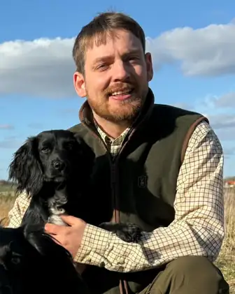 Kasper Selmar Pedersen sidder i marken med sin sorte cocker spaniel i armene